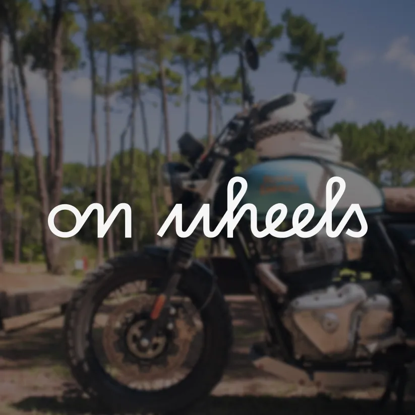 Logo blanc On Wheels appliquée sur une photo de moto en extérieur.